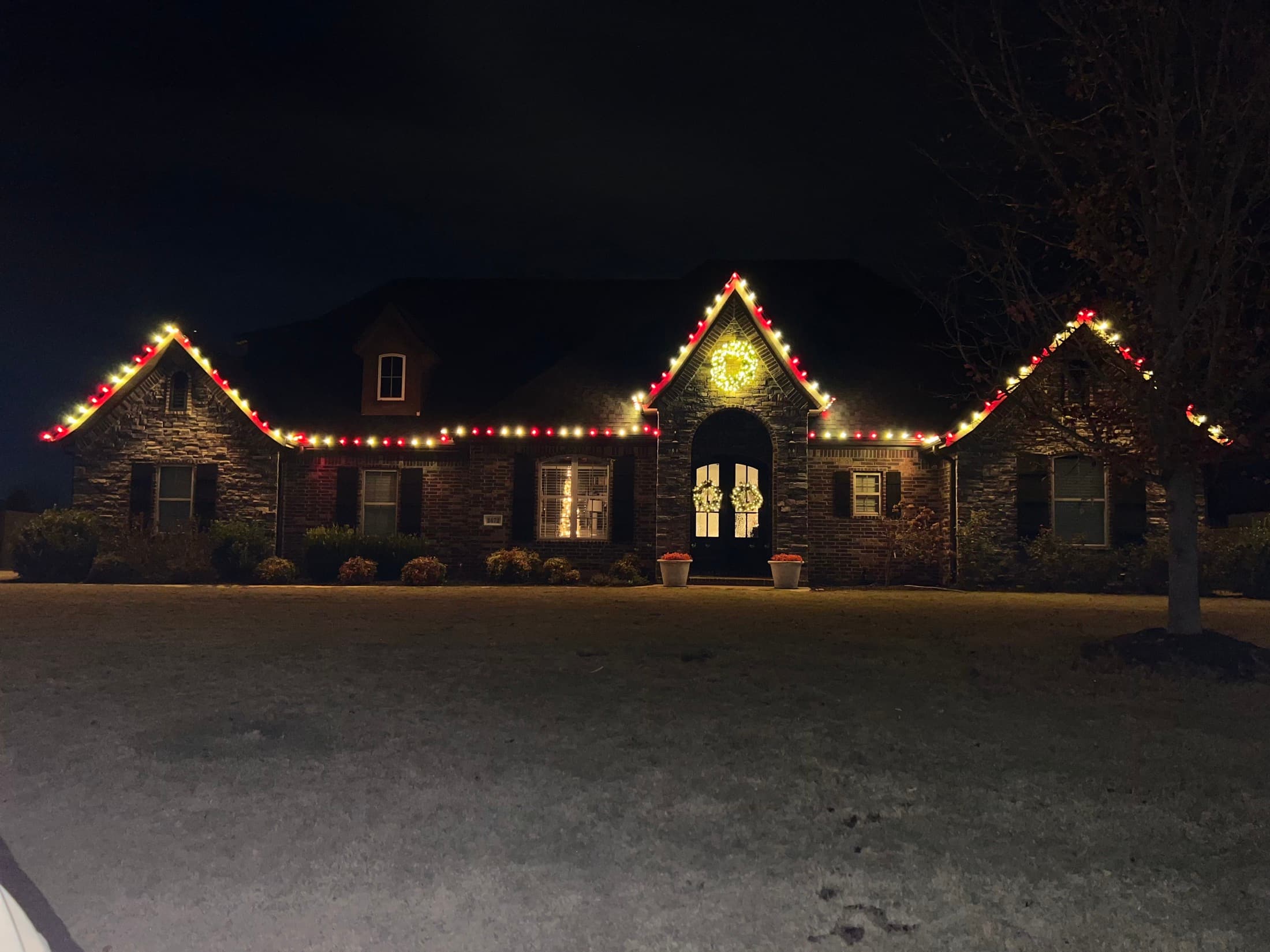 Red and warm-white custom holiday lighting across a stone and brick home